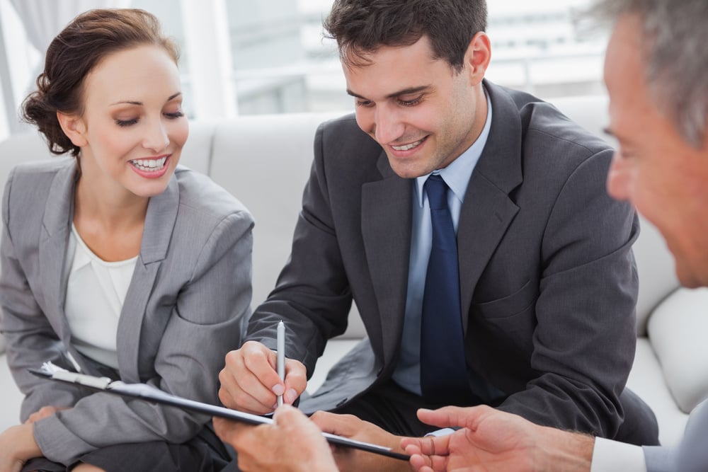 Businessman signing contract while his partner is looking at him in cosy meeting room